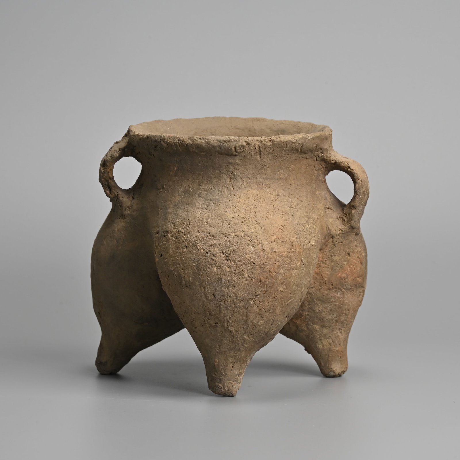 A CHINESE NEOLITHIC GREY POTTERY HANDLED TRIPOD VESSEL, LI, CIRCA 2ND MILLENNIUM BC.: A CHINESE NEOLITHIC GREY POTTERY HANDLED TRIPOD VESSEL, LI, CIRCA 2ND MILLENNIUM BC. A cooking vessel with three wide udder shaped legs allowing it to be stood in a fire, with two strap handles. 15.5c