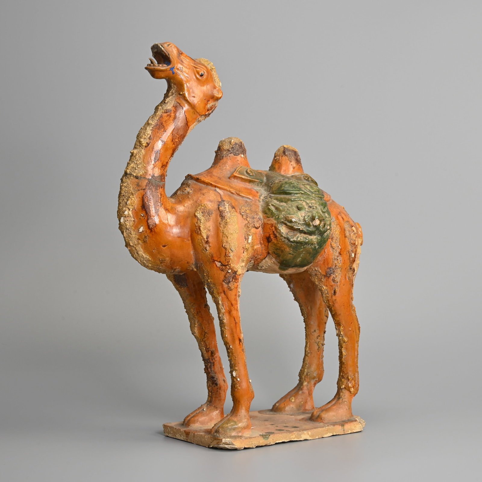 A CHINESE AMBER AND GREEN GLAZED CERAMIC MODEL OF A BACTRIAN CAMEL, TANG DYNASTY STYLE BUT 20TH: A CHINESE AMBER AND GREEN GLAZED CERAMIC MODEL OF A BACTRIAN CAMEL, TANG DYNASTY STYLE BUT 20TH CENTURY. Standing foursquare with its head raised upwards wearing a saddle bag. 44cm tall x 32cm length.