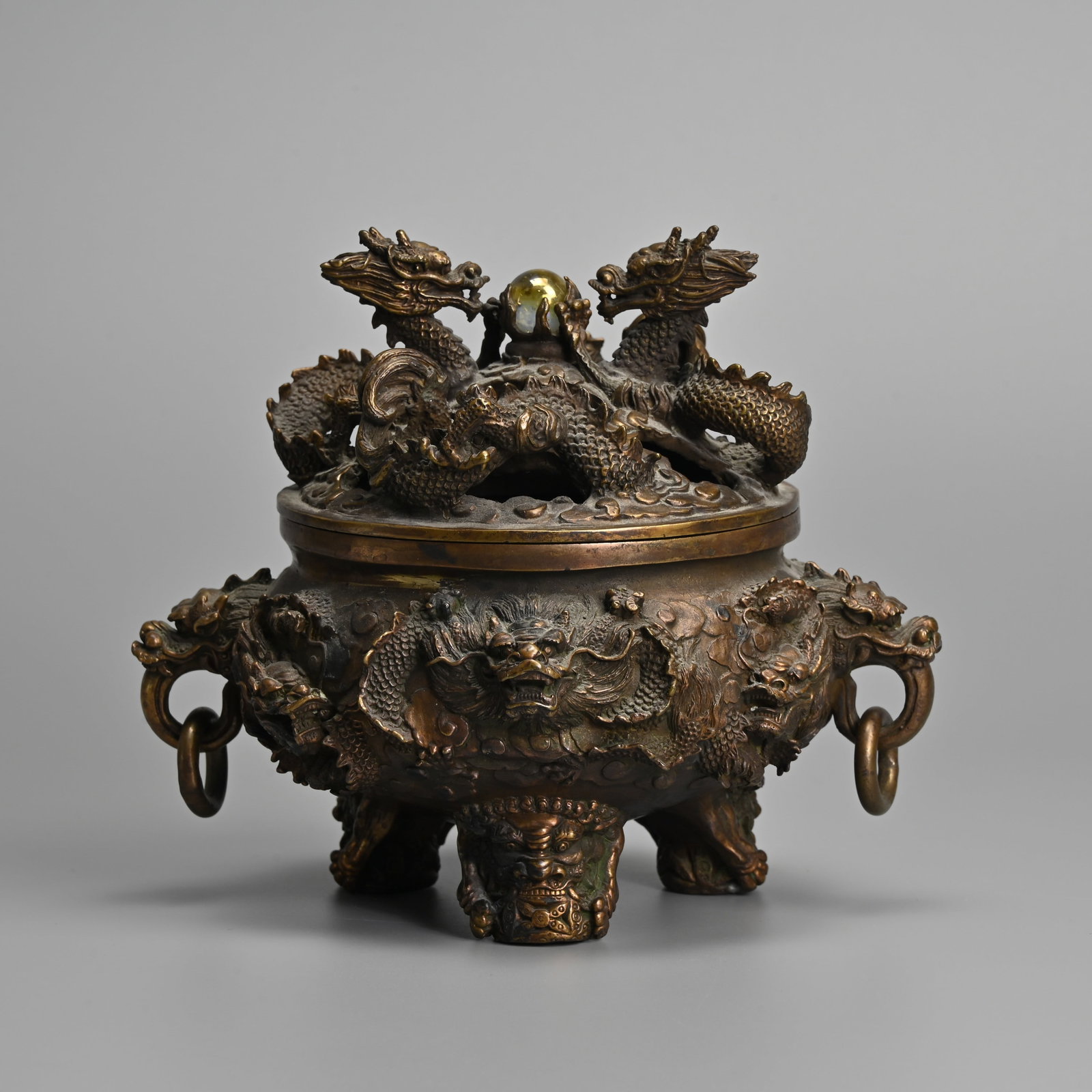 A JAPANESE BRONZE TRIPOD CENSER, KORO, 20TH CENTURY.: A JAPANESE BRONZE TRIPOD CENSER, KORO, 20TH CENTURY. Cast in relief with dragons amidst clouds, with dragon ring handles and lion feet. The cover featuring two dragons before a lustrous glass pearl. W