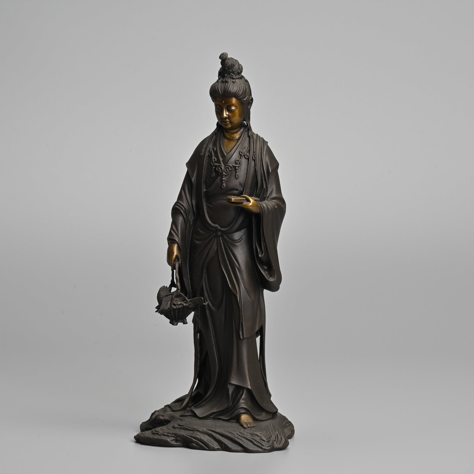 A JAPANESE PARCEL GILT BRONZE STANDING FIGURE OF GYORAN KANNON, AFTER TAKAMURA KOUN (1852-1934).: A JAPANESE PARCEL GILT BRONZE STANDING FIGURE OF GYORAN KANNON, AFTER TAKAMURA KOUN (1852-1934). The bodhisattva depicted holding a fish basket in her right hand. Signed in an impressed seal on the ba