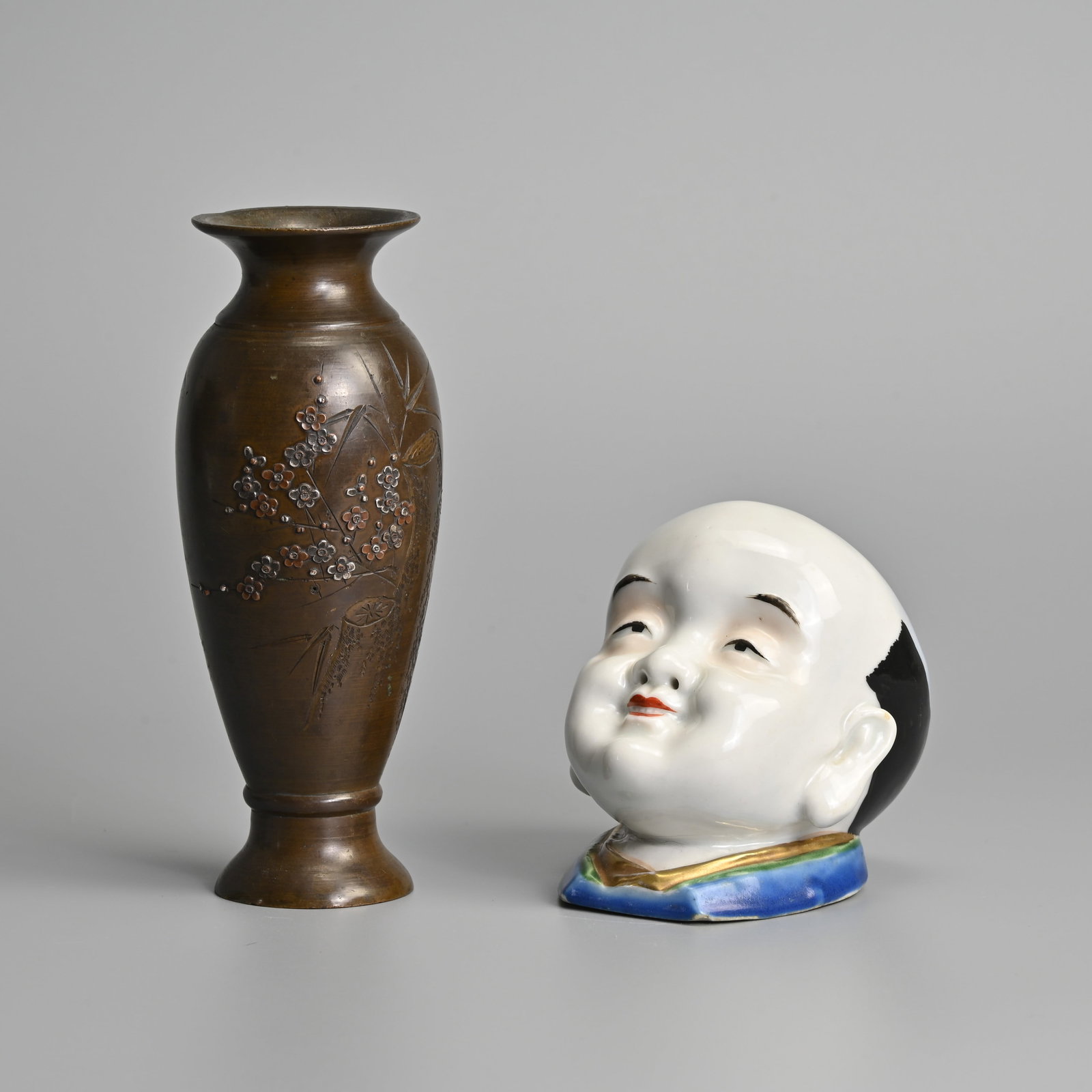A JAPANESE MIXED METAL VASE TOGETHER WITH A PORCELAIN POT MODELLED AS A HEAD, EARLY 2OTH CENTURY.: A JAPANESE MIXED METAL VASE TOGETHER WITH A PORCELAIN POT MODELLED AS A HEAD, EARLY 2OTH CENTURY. The vase incised and relief decorated with tree trunk and flowering bamboo branches; Together with a h