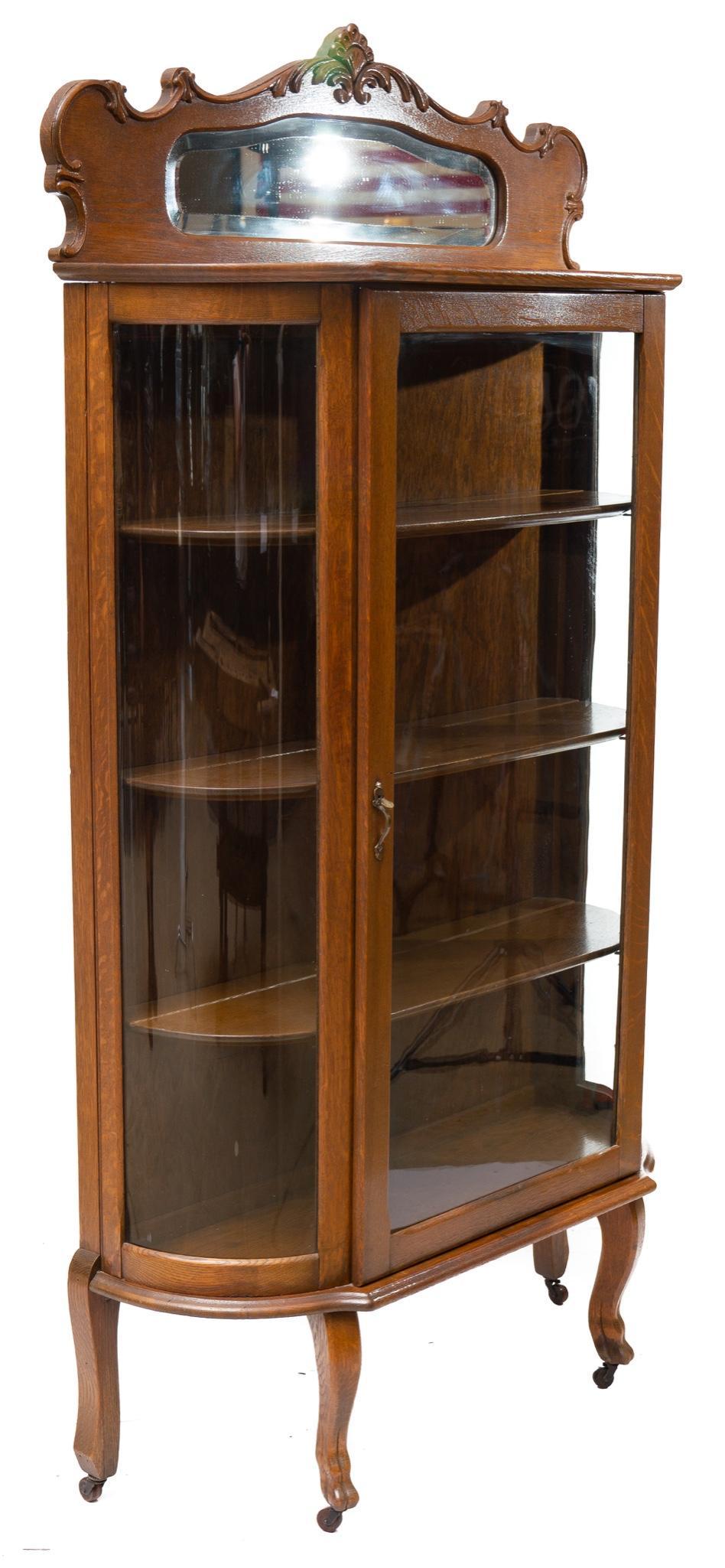 American Colonial-Style Curved Glass China Cabinet: Provenance: A New Braunfels, TX Estate Early American Colonial-style curved glass china cabinet, carved mantle, mirrored mantle accents, hoof feet 69.5" tall x 37" wide x 14" deep State-wide delivery 