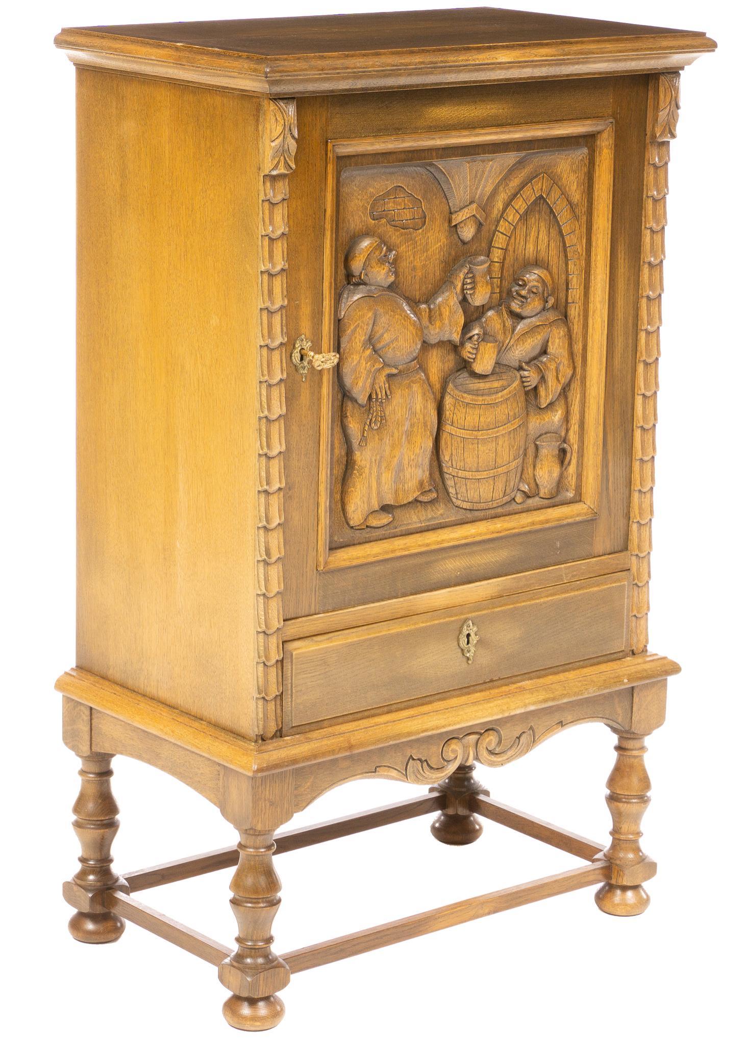 Heavily Carved Cabinet with Monk Scene: Cabinet, featuring a carved figural scene of two drinking Catholic monks, single door opens to shelved interior, above single drawer, rising on stretchered turned legs, includes key 43.5"h x 26.5"w x 