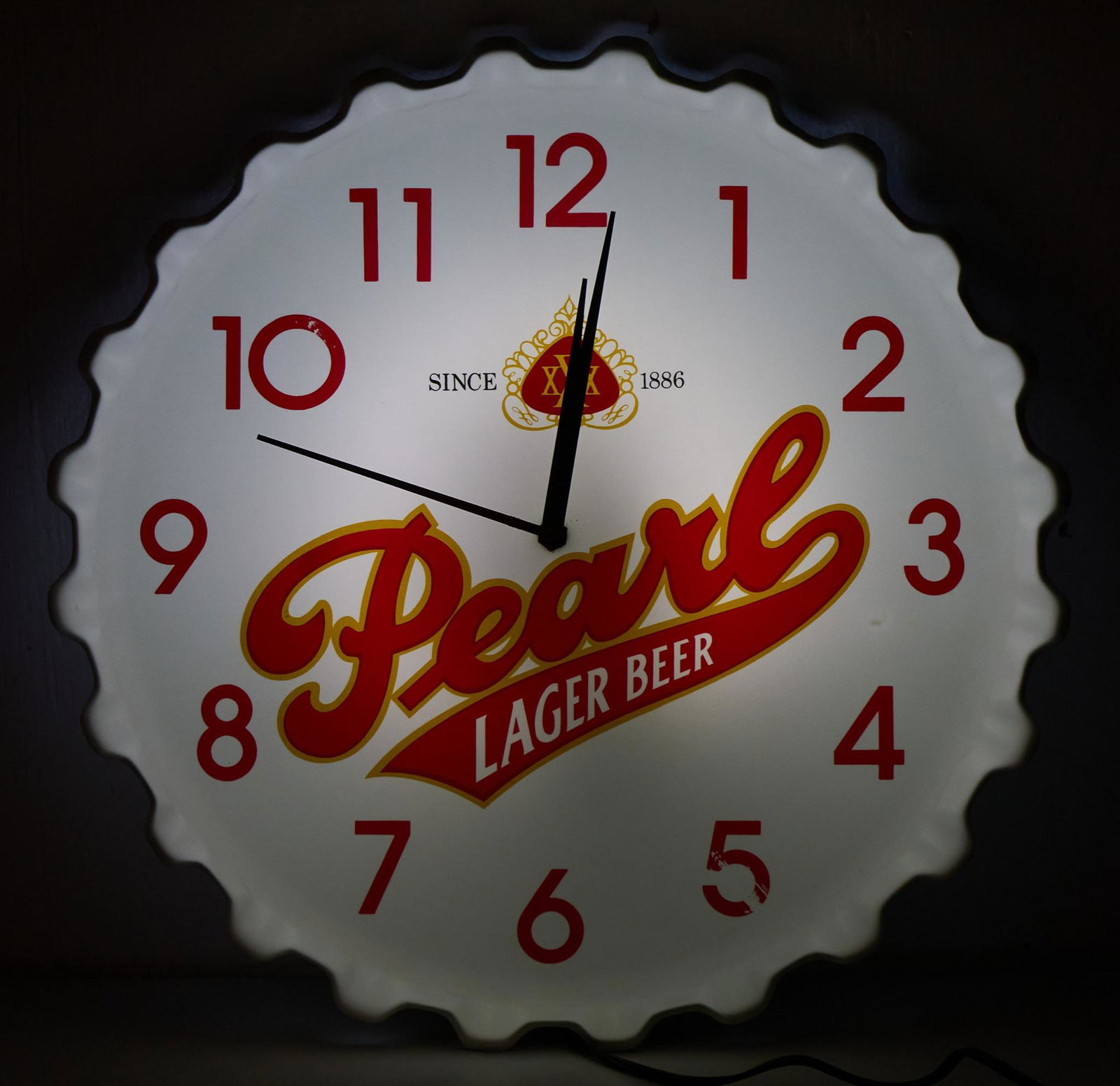 1983 Pearl Beer Bottle Cap Clock: Pearl Beer bottle cap illuminating advertising clock, featuring classic red and gold XXX logo with stylized lettering, marked Mirro 1983, in working condition 2.5"w x 18"d Provenance: A Seguin, Texa