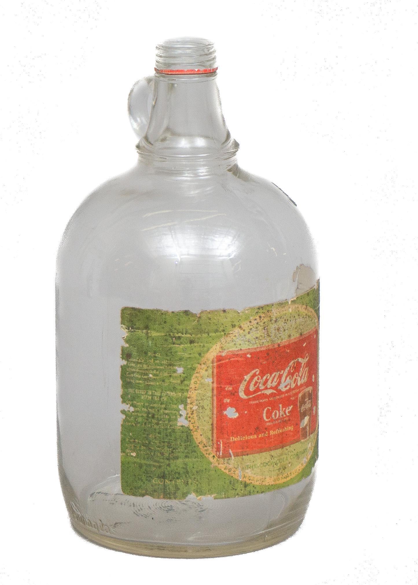 Glass Coca-Cola Syrup Jug: Vintage glass Coca-Cola syrup jug with color printed label featuring classic advertising logo on adhesive label 12.5"h x 6"d Provenance: The Estate of Glenn Terpin, San Antonio, Texas We happily provi