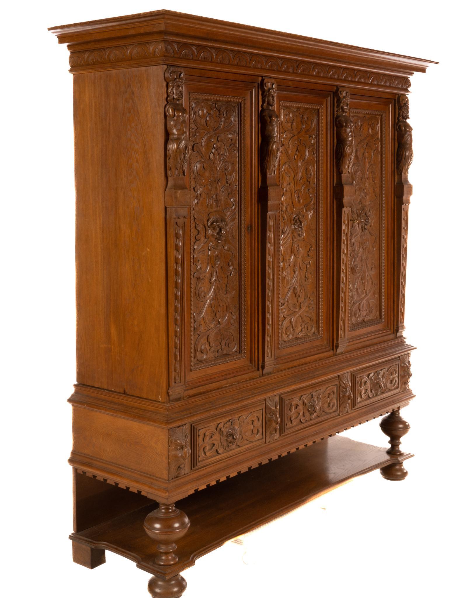 Renaissance Revival Cabinet: Renaissance revival cabinet, having heavily carved doors with triton motif, flanked by nymph pilasters, leading to interior shelving, above drawers, crenelated apron, rising on turned bun feet, to inc