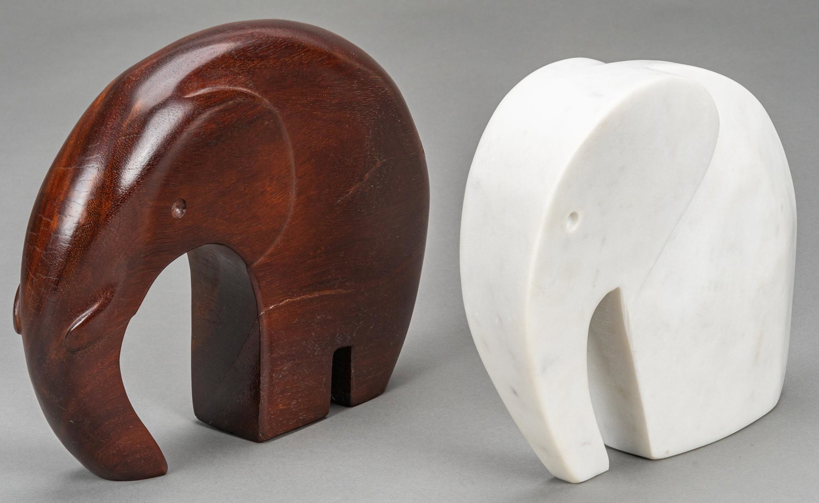 Pair of Minimalist Carved Elephant Statues: Pair of minimalist decorative elephant statues, one carved from wood, the other marble height 8.5 in. x width 10.5 in. x depth 2.5 in. / largest Provenance: A Rockport, Texas collection We happily pro