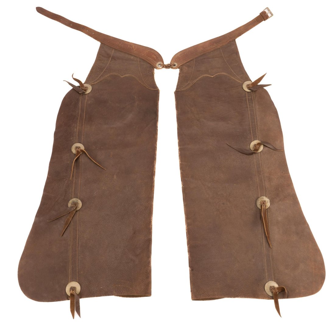 Early Style Bat Wing Chaps: Early style brown leather bat wing chaps, with large slotted conchos, with stitched decoration, scratched lettering on billet length 42 in. Provenance: An Alamo Heights, Texas collection We happily pr