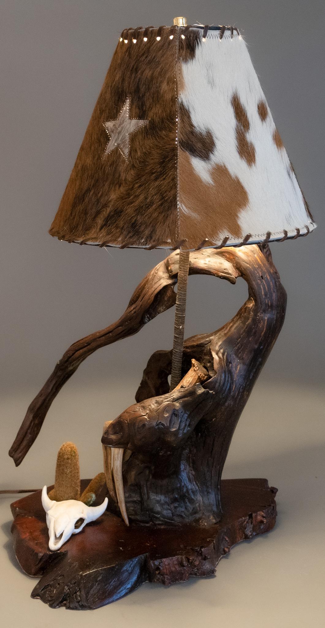 Rustic Live Edge Table Lamp: Rustic live edge lamp, having cowhide lampshade, with perforated accents and star motif, supported on rebar base, encircled with unfinished log, supported on wooden slab base, with faux taxidermy and 