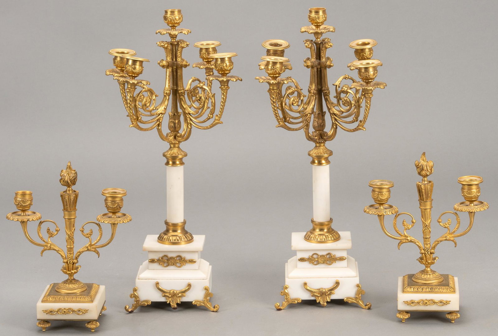 Set of (4) Louis XVI Style Gilded and Marble Candelabras: Set of four (4) Louis XVI style garnitures to include two taller centerpieces with gilded candelabra atop marble base, with two matched smaller examples height 19.5 in. x width 8 in. x depth 8 in. / l