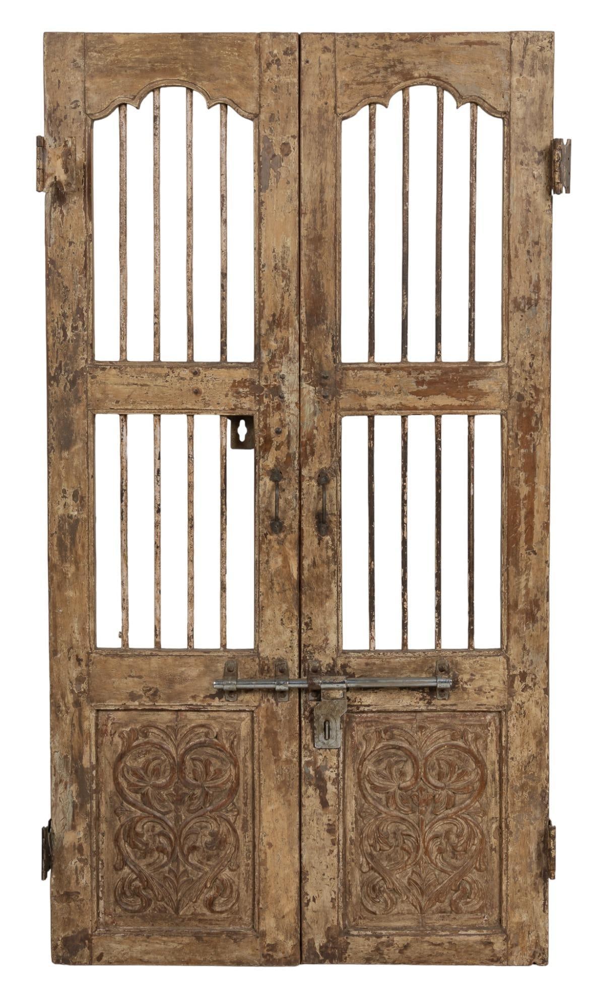 Pair of Architectural Doors: Pair of architectural teak doors, featuring carved filigree motif on lower panels, with iron accents and hardware, with recently replaced bar for sliding latch lock, and remnants of white paint height