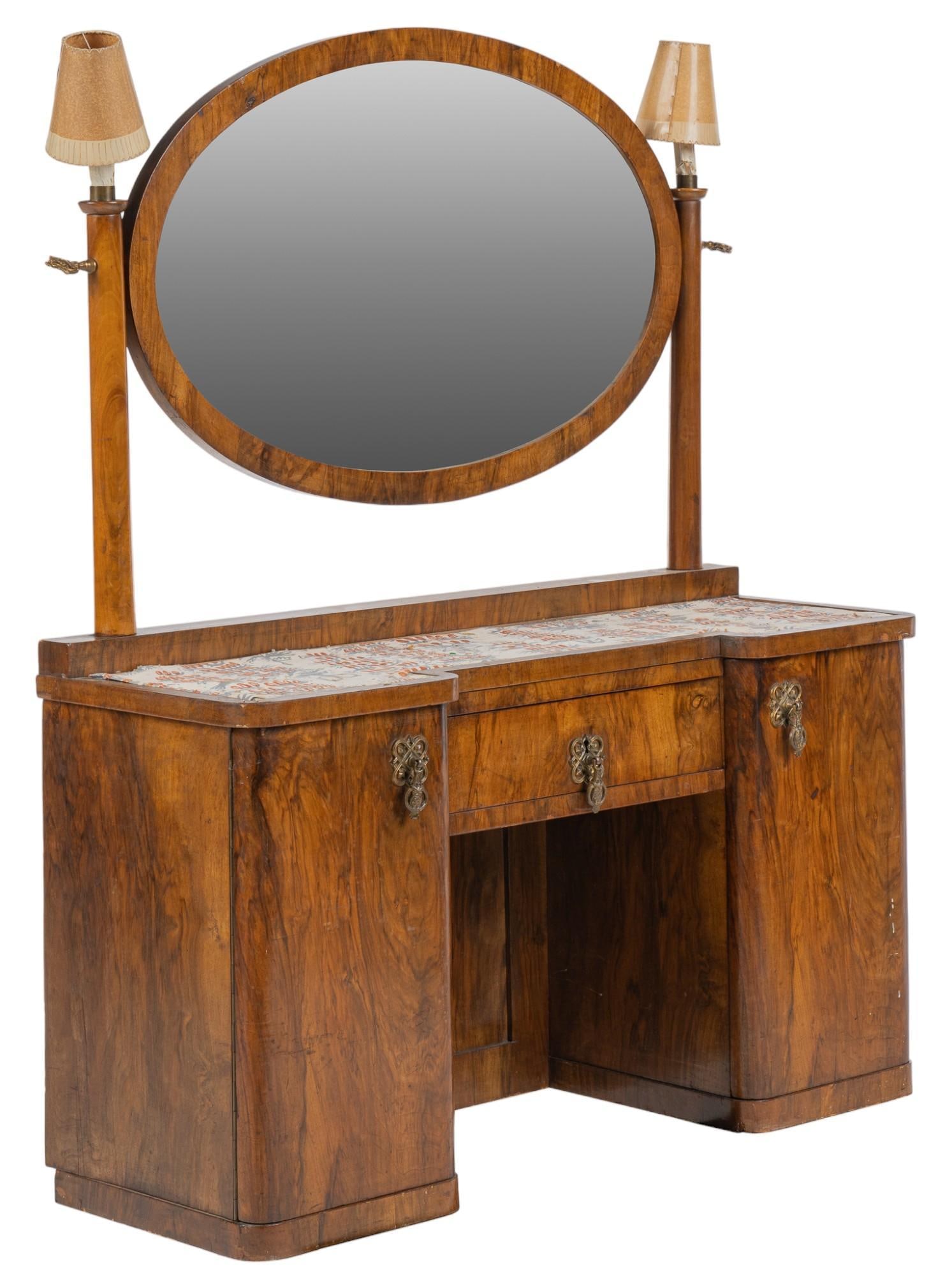 Vintage Bedroom Vanity: Vintage bedroom vanity with ovular mirror in wooden frame, with supported crowned with shaded lighting fixtures, above lower desk section lined with fabric, above central drawer with metal pull, flank