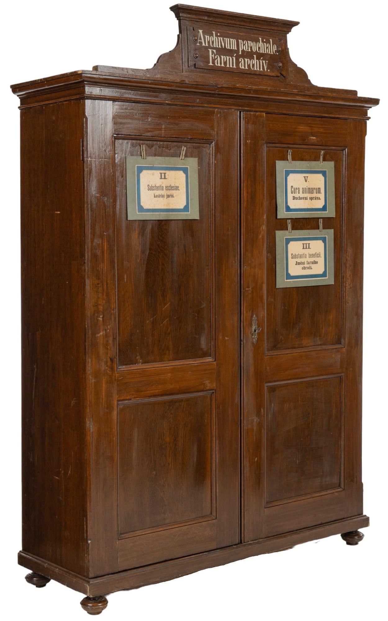 Czech Parish Wardrobe: Large wood wardrobe, featuring removable crown, and adorning labels in Czech language, describing parish, and religious topics, such as "Parish Archive" on crown piece, with pair of cabinet do