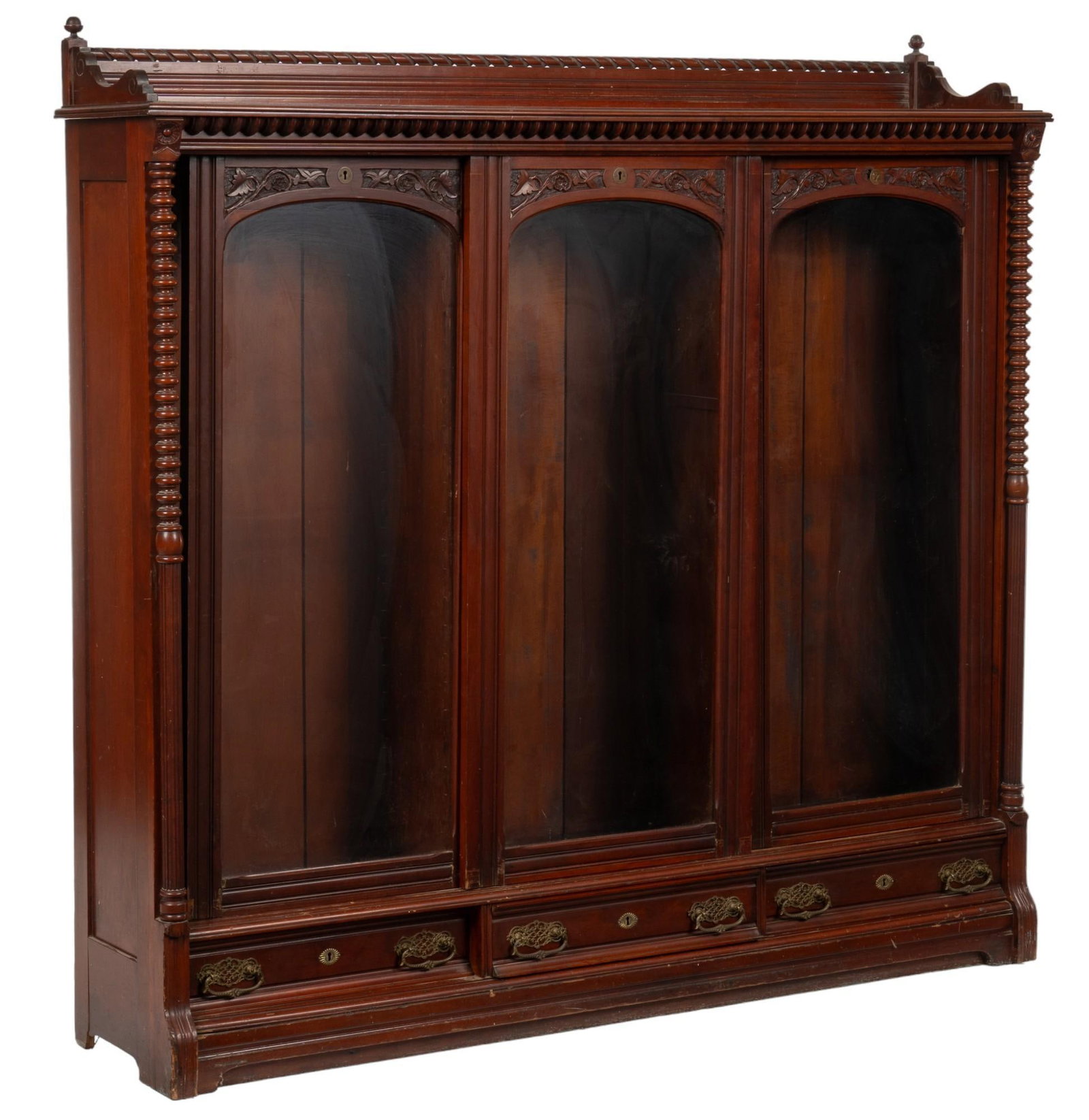 Sliding Door Cabinet: Carved wood cabinet featuring gallery with carved accents and finials, above three sliding cabinet doors with carved leaf and vine motif, that open to interior storage, flanked by turned and fluted pi