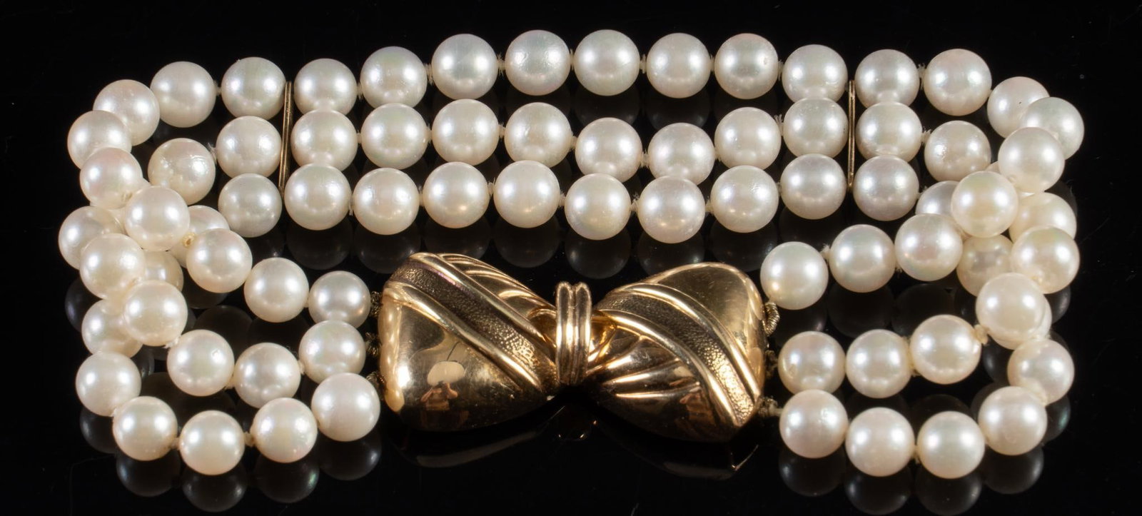 Pearl and 14K Gold Bracelet: Pearl and 14K gold bracelet, three strings of pearls, pearl diameter 2.0 mm, 14K gold bow shaped clasp, marked "14K" Circumference: 7.5 in Total weight: 15.4 g Provenance: Property from the es