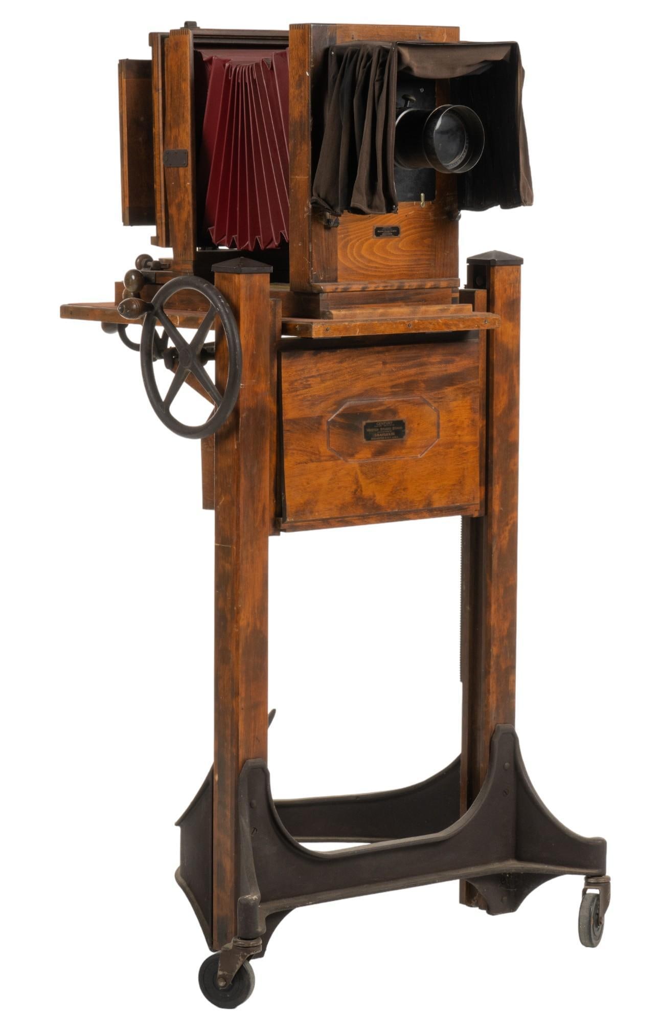 Antique Century Master Sliding Carriage Camera: Antique Sliding Carriage master studio camera for Century Master Studio, manufactured by Graflex, Inc. (Rochester, New York), with crank adjustment, and wooden frame supported on metal base with wheel