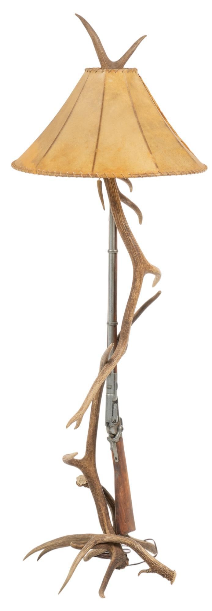 Antler and Rifle Floor Lamp: Ranch style floor lamp, featuring deer antlers, with hunting rifle accent, and hide shade with whip stitch edge height 72 in. x width 19.5 in. x depth 24 in. Provenance: Property from the monumental l