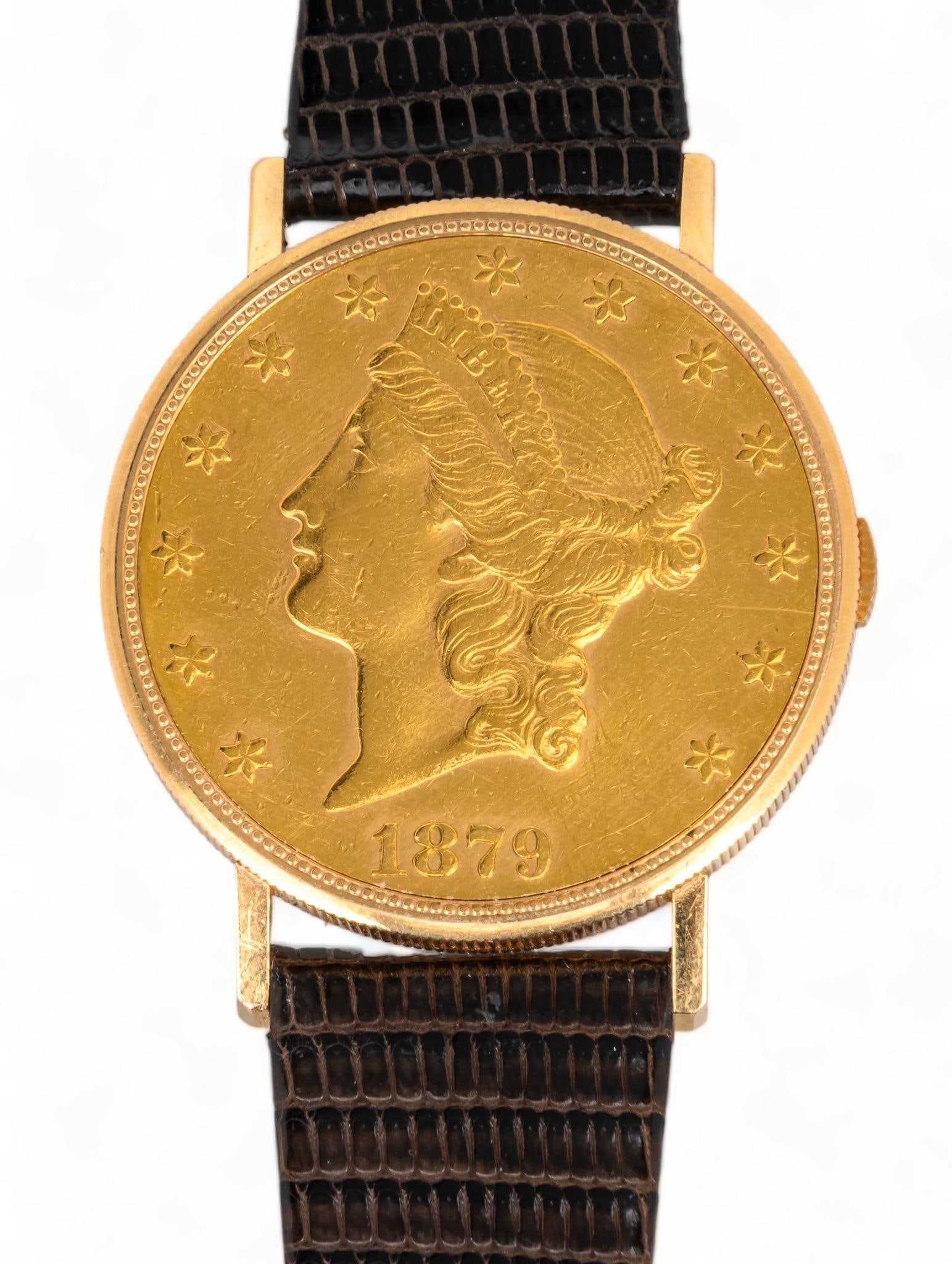 1879 $20 Gold Liberty Coin Watch: Eska 18k gold watch hinged inside hollowed 1879 $20 US gold coin on leather strap, marked case / diameter 34 mm. length 7 in. - 8.5 in. Provenance: Property from a luxury condominium in the Alamo Heig