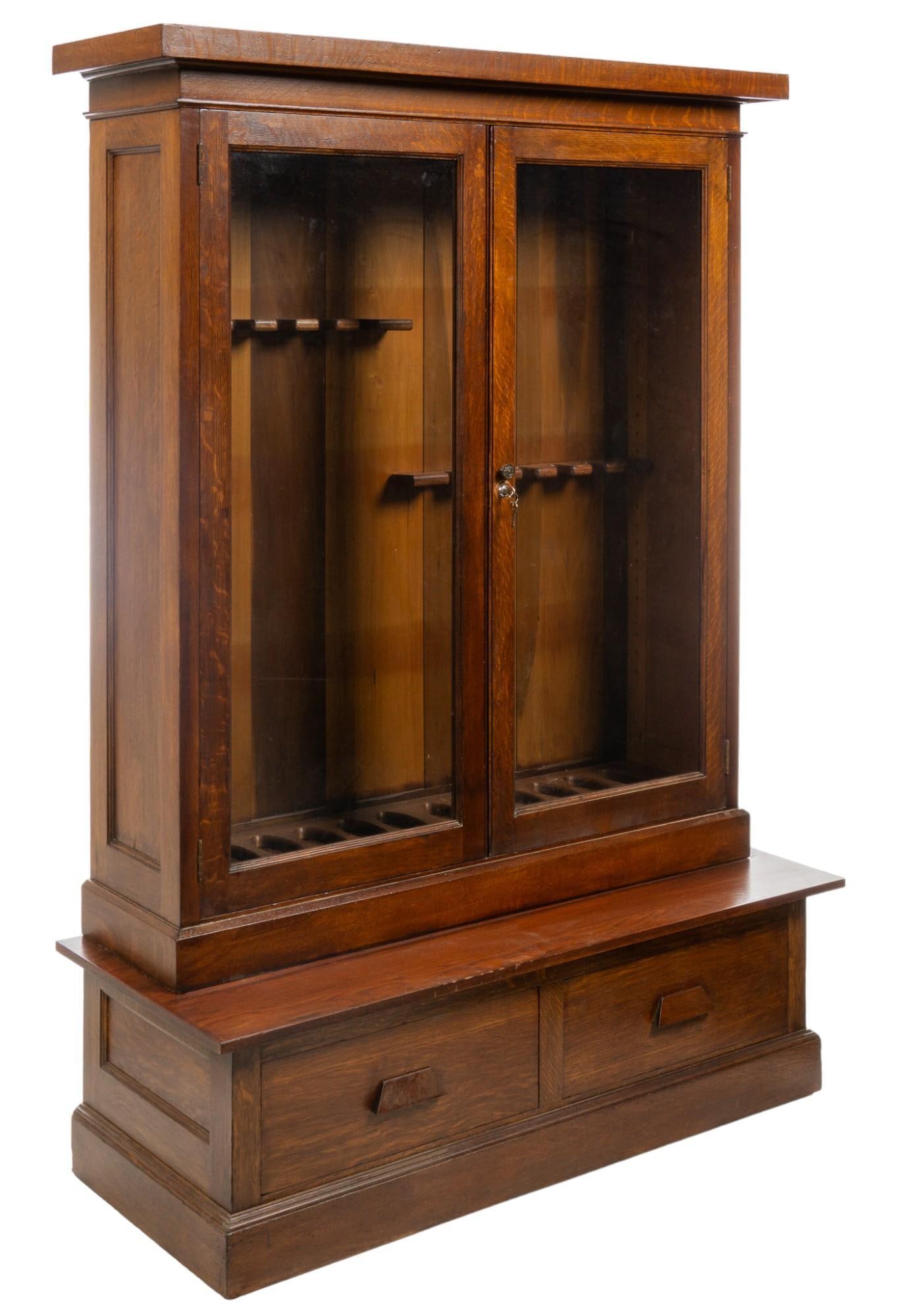 Gun Cabinet: Wooden gun cabinet featuring top section with pair of glass doors that open to internal storage equipped to store twelve rifles, supported on separate base piece equipped with pair of large drawers wi