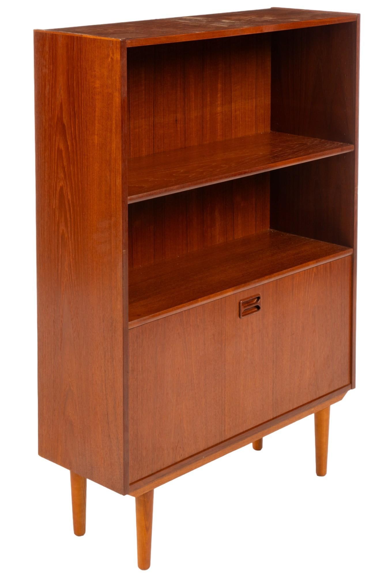 Danish Mid-Century Bookcase: Danish mid-century bookcase single shelf above cabinet door that drops to reveal curved shelf beside two storage spaces, supported on pin legs height 49 in. x width 34 in. x depth 12 in. Shipping avai