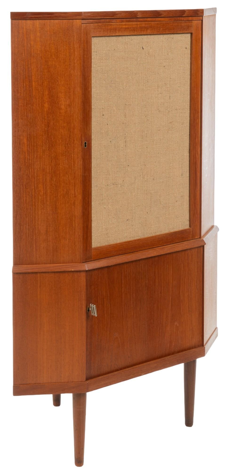 Danish Mid-Century Corner Cabinet: Danish mid-century corner cabinet featuring paneled door with key clock, clad in burlap that opens to interior storage with single shelf, above key lock cabinet door that opens to interior storage, su