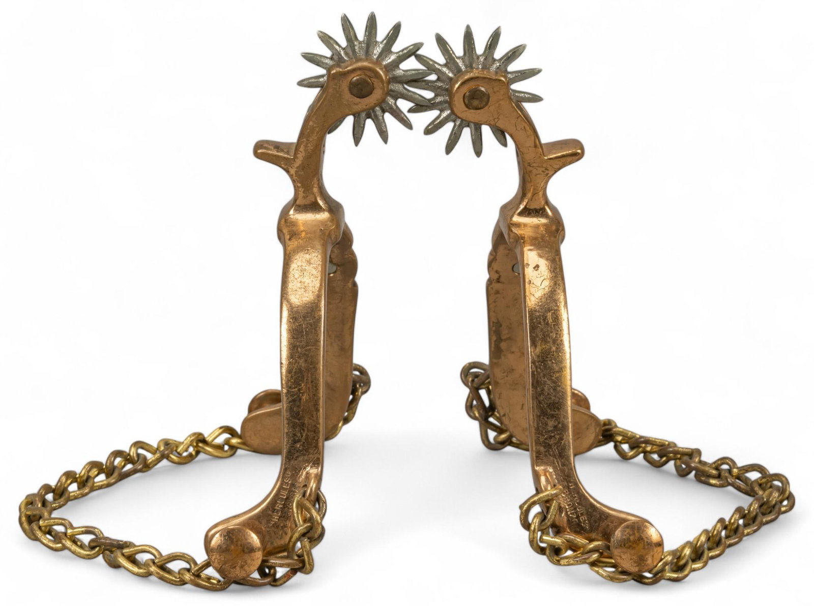 Pair of Hercules Bronze Star Marked Cowboy Spurs: Pair of Hercules bronze star marked cowboy spurs featuring floral engraved details on heel band and shank, fourteen point rowels, heel chain, no leather strap, marked "Hercules Bronze" height 