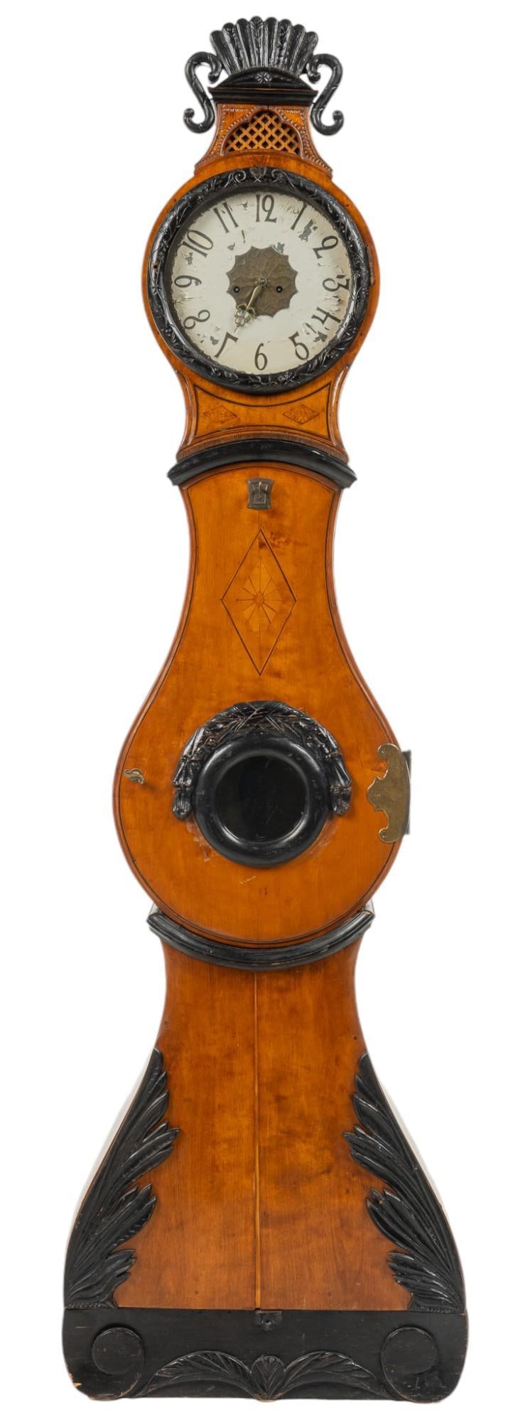 French Walnut Morbier Floor Clock: French walnut Morbier floor clock, wooden case, with black embellishments throughout, decorative carvings on sides, unmarked clock face height 86 in. x width 25 in. x depth 8 in. Provenance: Property 
