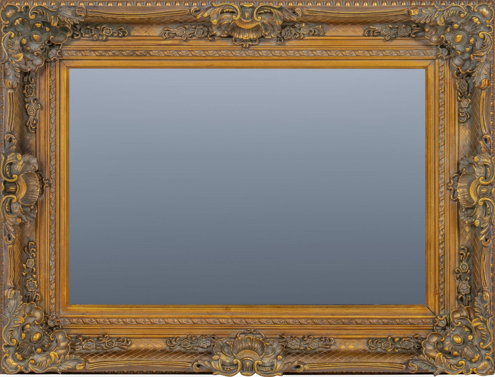 French Giltwood Wall Mirror: French wall mirror with heavily carved wooden frame featuring intricate scrollwork, with floral motifs, and golden finish, circa 1920-1930s height 37.5 in. x width 43 in. x depth 4 in. Provenance: