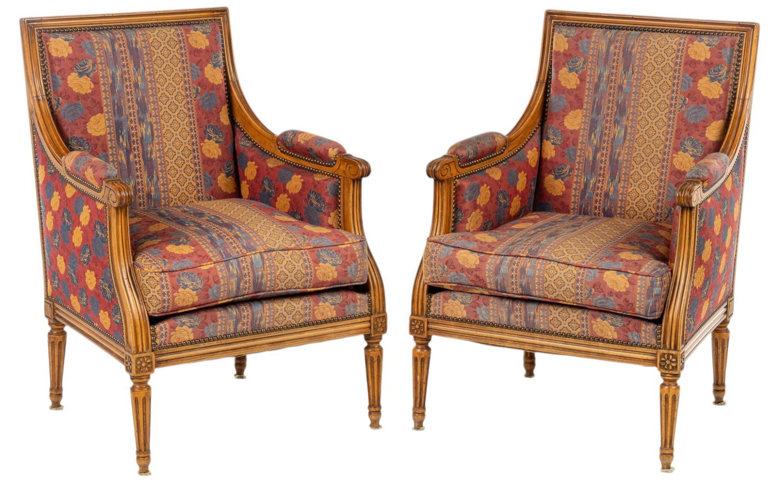 Pair of Upholstered Armchairs: Pair of upholstered armchairs, with cushioned seat and armrests, carved wooden frame, metal rivets throughout, on carved tapered pin legs with floral motifs height 36 in. x width 25 in. x depth 24 in.
