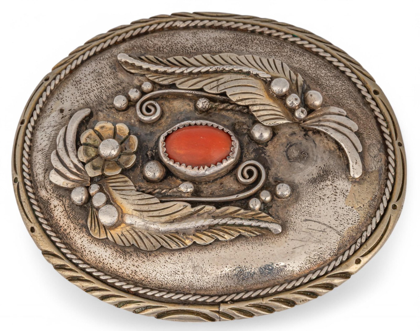 Sterling Silver Coral Belt Buckle: Sterling silver coral belt buckle featuring single inlaid coral piece with floral soldered details, marked with symbol length 3.25 in. x width 2.5 in. Total weight: 1.84 ozt Provenance: Property from 