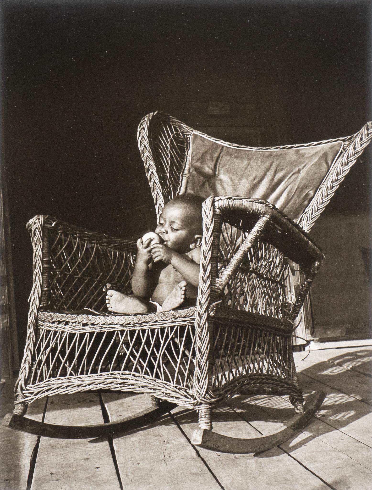 Ferne Koch, Infant in Chair: Ferne Koch (1923-2011, Texas) signed black and white photograph of an infant in wicker rocking chair, holding an apple sight: 13 x 10 in., frame: 21 x 17 in. Provenance: Property from the collection o