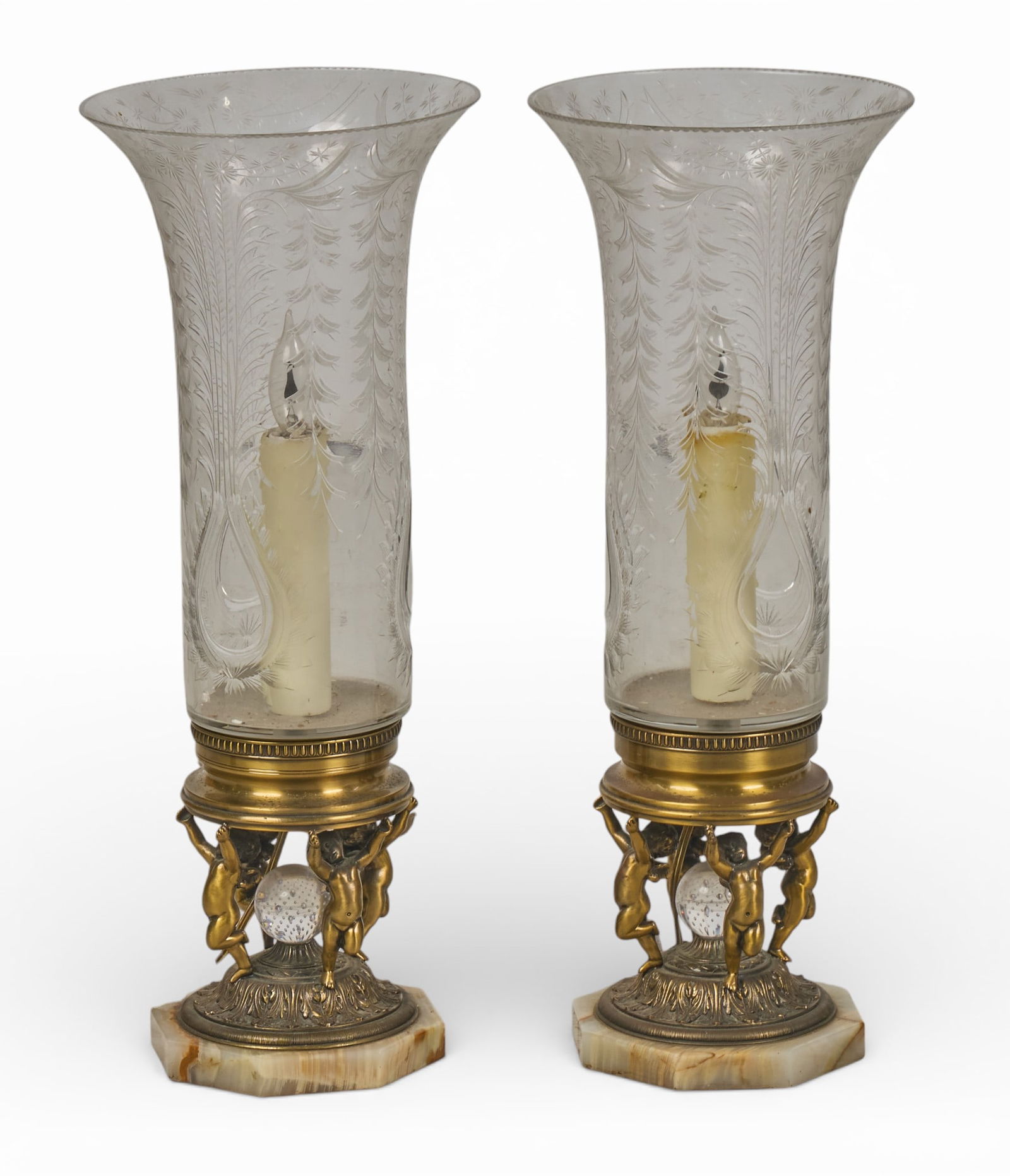 Pair of Etched Glass Lamps: Pair of etched glass hurricane lamps, each with a brass base featuring cherub figures and a crystal ball, on hexagonal marble base height 21 in. x width 8.5 in. x depth 8.5 in. / each Provenance: