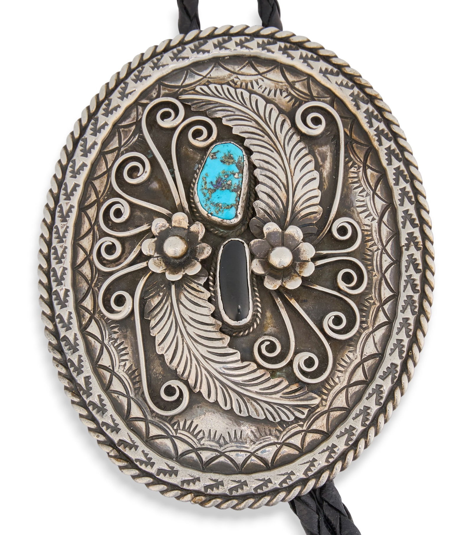 Raymond Clark, Navajo Turquoise & Onyx Bolo Tie: Navajo sterling silver bolo tie, with inlaid turquoise and onyx, and featuring twisted rope and foliate motifs, on braided black leather cord, marked "Raymond Clark Navajo" Length: 40 in.Pen