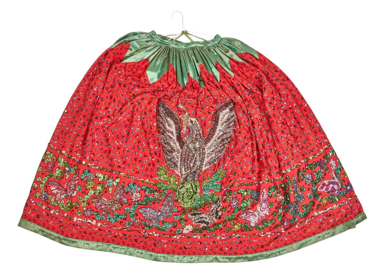 Vintage Mexican China Poblano Skirt: Vintage Mexican china poblano dancing skirt of red fabric and green satin trim, with numerous hand-sewn glass beads arranged in floral motifs, and depicting Mexican Coat of Arms, with two hook cl