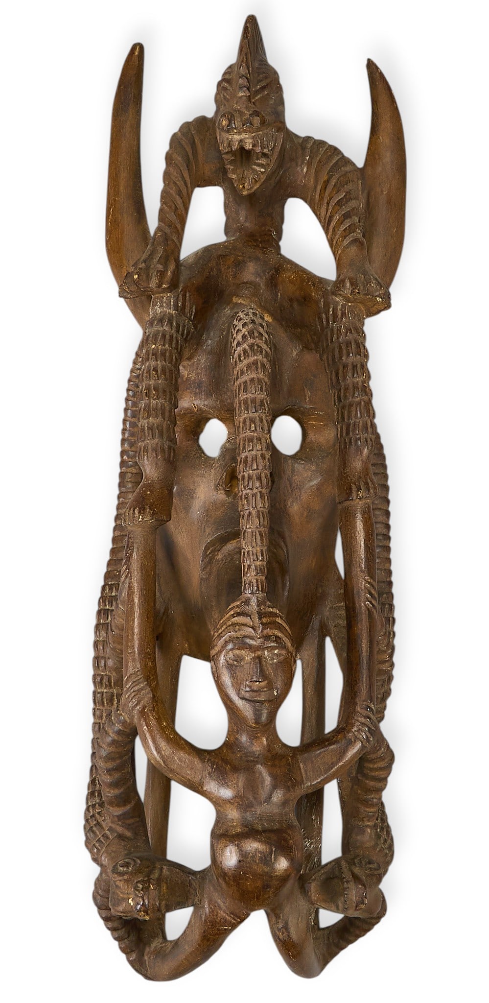 Carved Mexican Folk Art Mask: Carved wooden Mexican folk art mask featuring a central face with pierced eyes, flanked by carved figures and snakes height 27 in. x width 9 in. x depth 7.5 in. Provenance: Property from a home in Lar