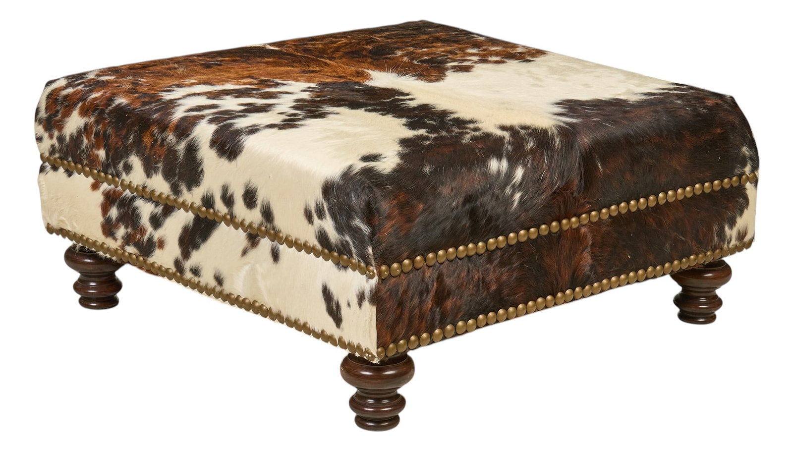 Cowhide Ottoman: Fairfax Design, Inc. (Dallas, Texas) handcrafted cowhide ottoman, with brass nailhead trim and turned wooden feet height 18 in. x width 38 in. x depth 38 in. Provenance: Property from the