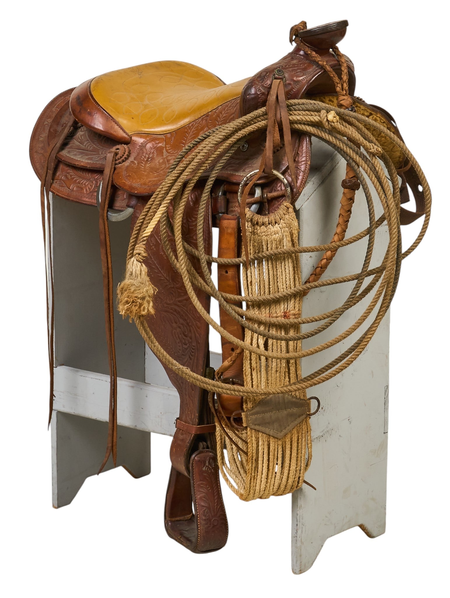 Leather Saddle: Vintage Western riding leather saddle with tooled decoration, leather pommel and stirrups, and lasso, stand not included height 40 in. x width 22 in. x depth 26 in. Provenance: Property from a h