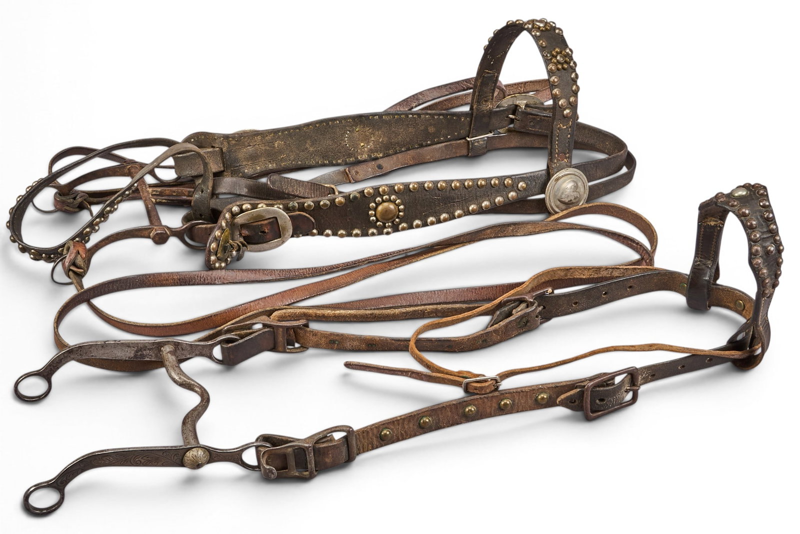 (2) Vintage Leather Bridles: One early Mexican bridle with silver bit, and one studded cowboy bridle with early heart conchos height 7.5 in. x width 25 in. x depth 7.5 in. Provenance: Property from a home in San Antonio, Te