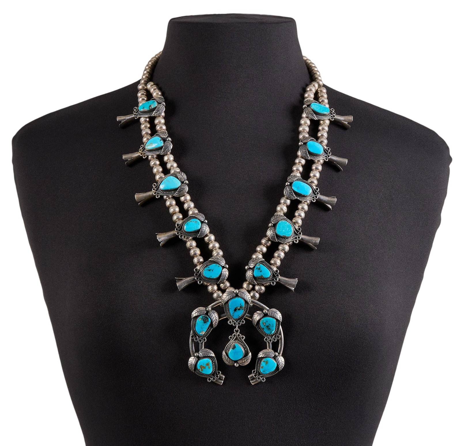 Navajo Sterling Silver & Turquoise Squash Blossom: Navajo sterling silver squash blossom necklace, set with turquoise cabochons throughout, featuring twisted rope and leaf motifs, with hook and eye closure Length: 27 in. Total weight: 169.2 g Pro