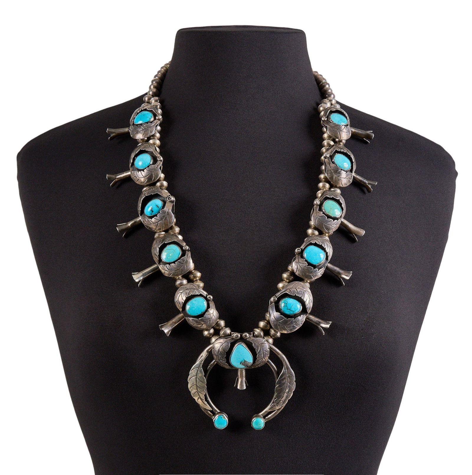 Sterling & Turquoise Shadowbox Style Squash Blossom: Sterling silver squash blossom necklace, set with turquoise cabochons in shadowbox style settings, featuring leaf motifs and stamped details, with hook and eye closure Length: 29 in. Total weight: 244