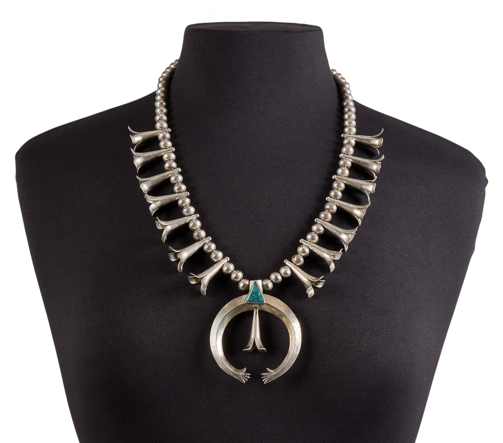Modernist Sterling Silver & Turquoise Squash Blossom: Modernist style sterling silver squash blossom necklace, set with single triangle-cut turquoise detail to naja, with hook and eye closure, signed to reverse Length: 25 in. Total weight: 182.0 g Proven