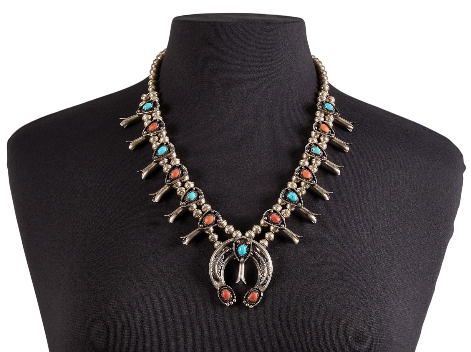 Petite Sterling Silver Turquoise & Coral Squash Blossom: Petite sterling silver squash blossom necklace, set with alternating turquoise and coral cabochons, featuring feather motifs, with hook and eye closure Length: 23 in. Total weight: 117.6 g Proven
