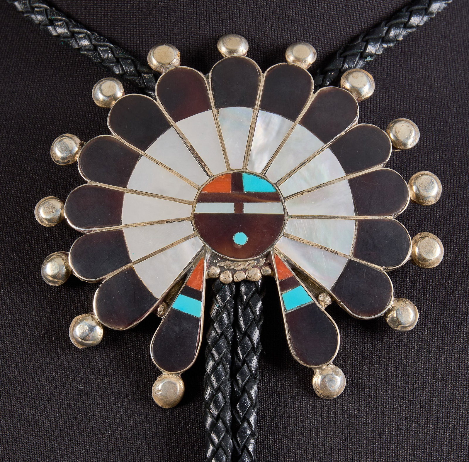 Thomas Boone, Zuni Sterling & Multi-Stone Bolo: Thomas Boone, Zuni sterling silver bolo tie, pendant set with multi-tone inlay featuring turquoise, coral, onyx, and mother of pearl, on braided black leather cord, signed "T. Boone Zuni"