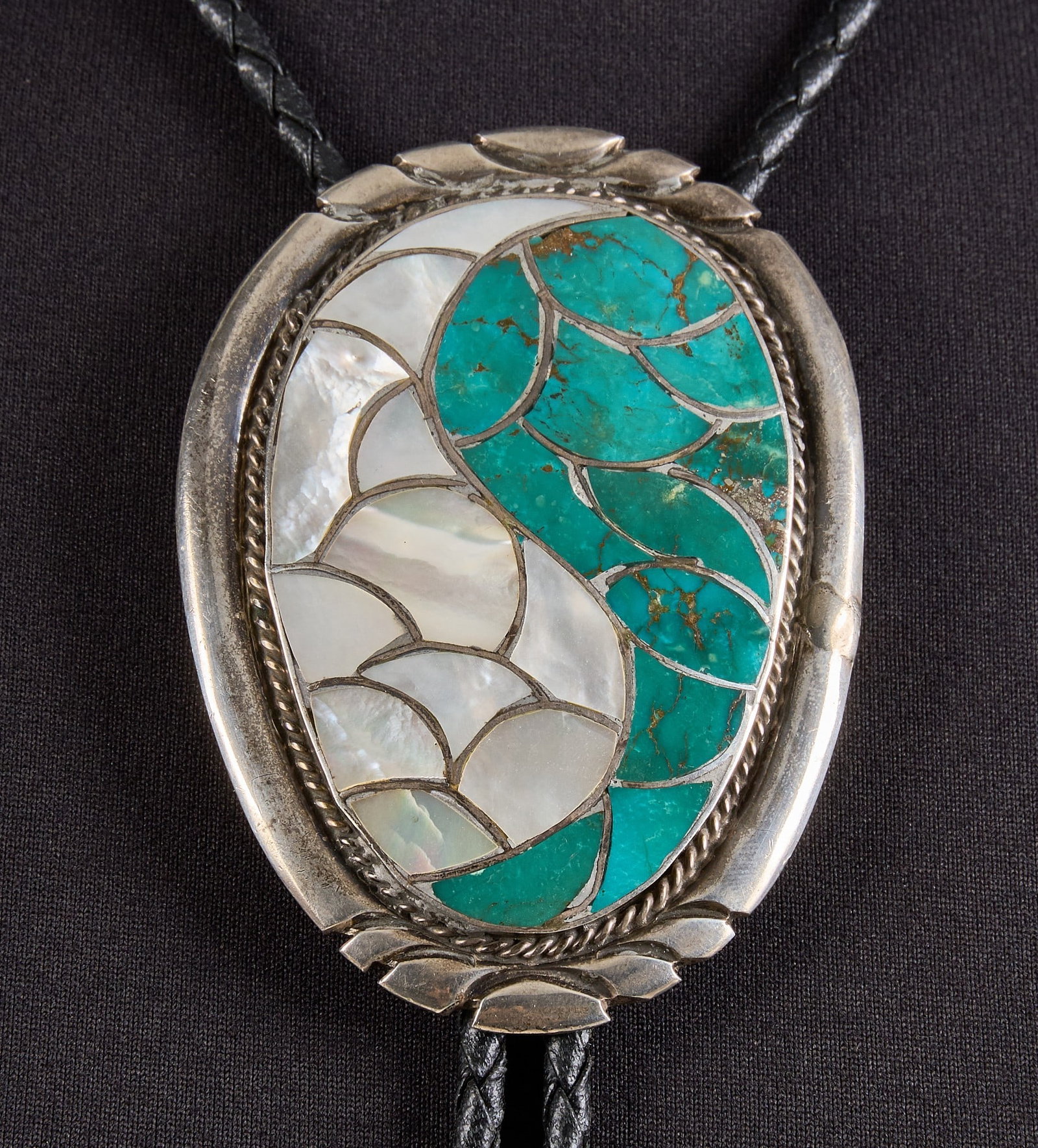 Sterling Silver & Multi-Stone Fish Scale Bolo: Sterling silver bolo tie, set with turquoise and mother of pearl inlay in fish scale design, with twisted rope motif and stamped details, on braided black leather cord Length: 41 in. Total weight