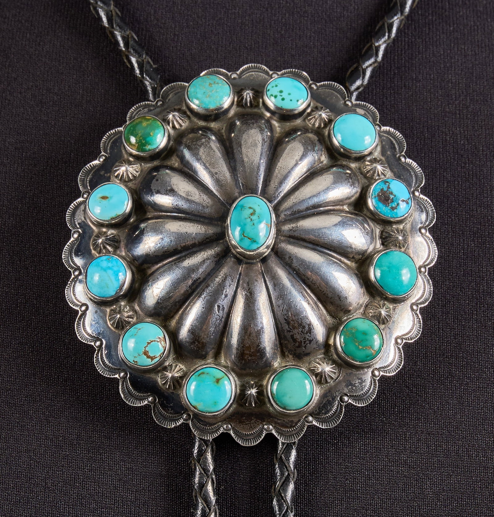 Southwestern Sterling Silver & Turquoise Bolo: Southwestern sterling silver bolo tie, set with turquoise cabochons in a cluster design, featuring stamped details to borer, on braided black leather cord Length: 38.5 in. Total weight: 84.7 g Pr
