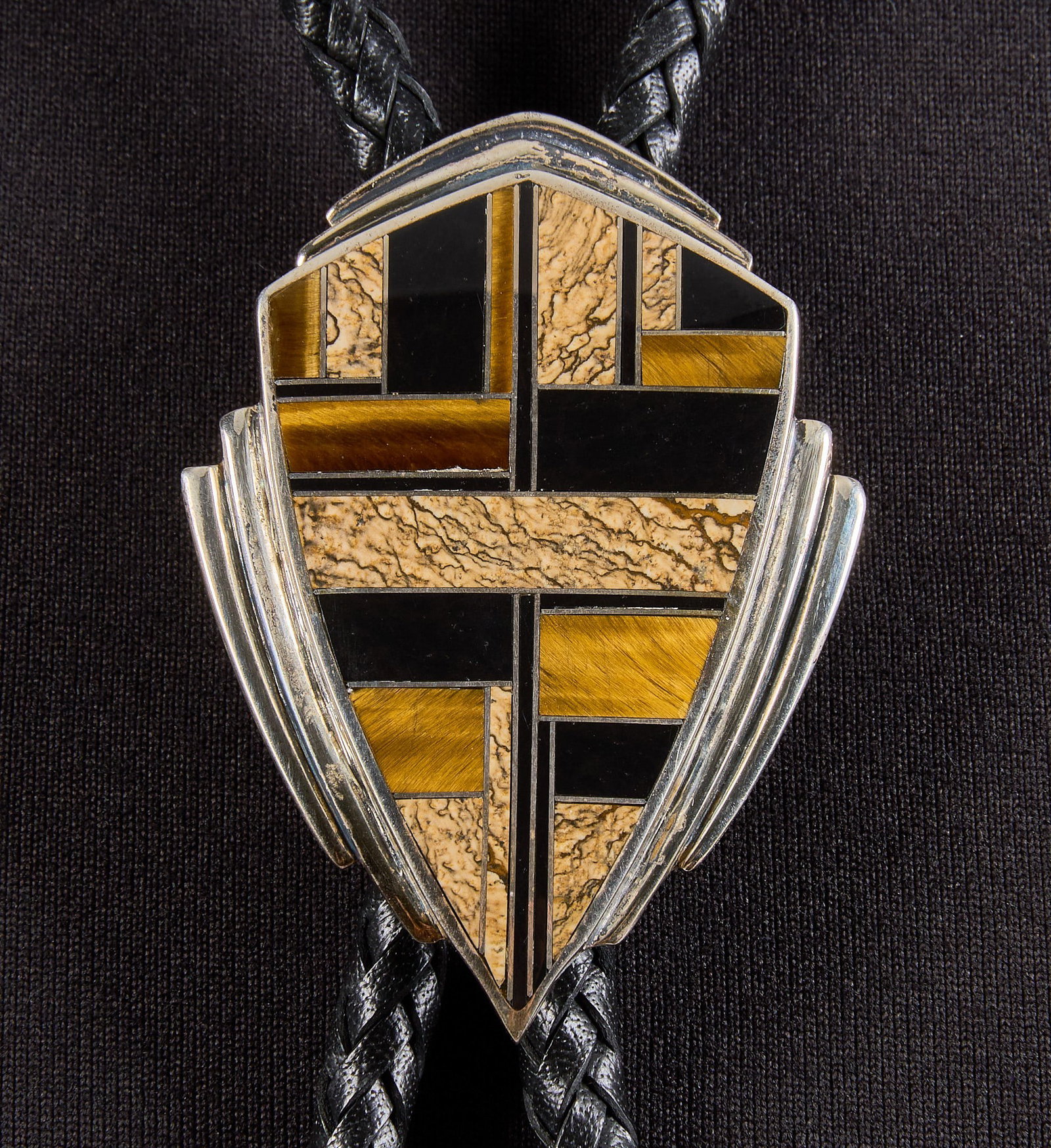 Sterling & Multi-Stone Inlay Bolo: Sterling silver bolo tie, pendant set with multi-stone inlay in geometric design, on braided black leather cord, marked "Sterling" Length: 45 in. Pendant: 1.75 in. x 2.5 in. T