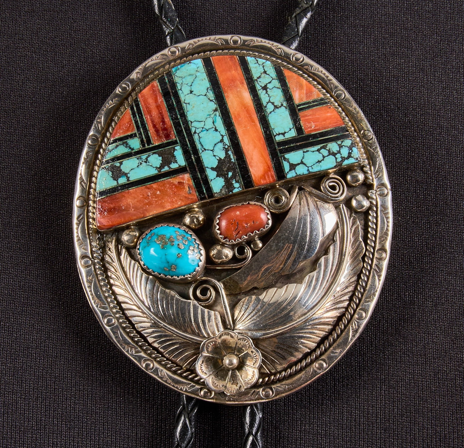 Sterling Silver Turquoise & Coral Bolo: Sterling silver bolo tie, set with turquoise and coral cabochons and inlay, featuring floral and twisted rope motifs, with turquoise and coral to aiguillettes, on braided black leather cord, marked &q