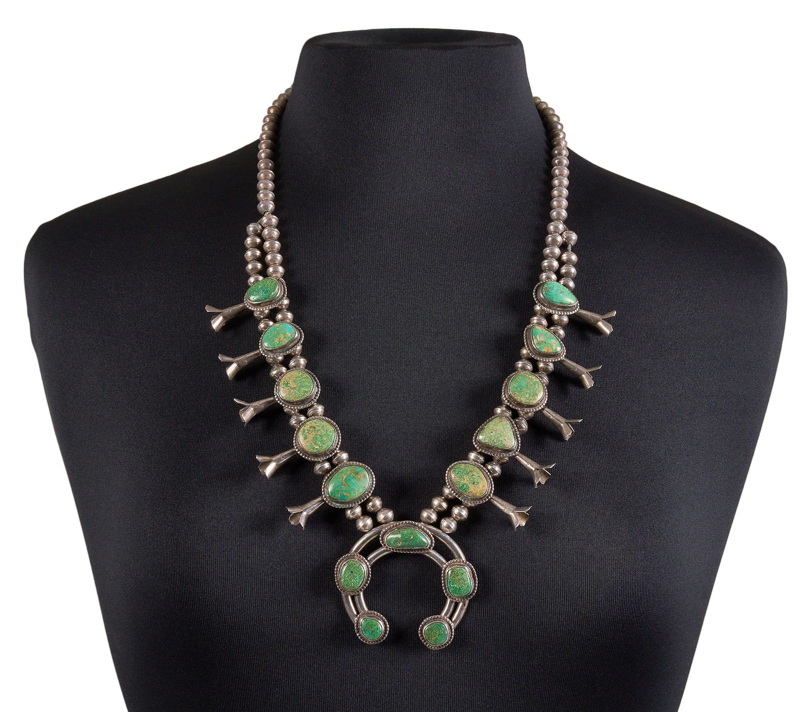 Sterling & Green Turquoise Squash Blossom: Sterling silver squash blossom necklace, set with green turquoise cabochons, with twisted rope motif style bezels, with hook and eye closure, signed "GG" Length: 28 in. Total weight: 16