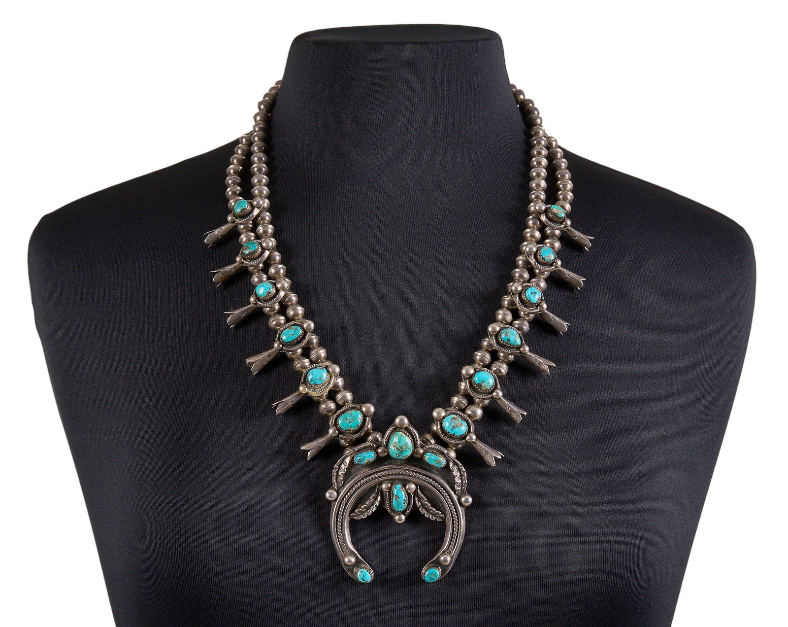 Navajo Sterling & Turquoise Squash Blossom: Navajo sterling silver squash blossom necklace, set with turquoise cabochons, featuring twisted rope and leaf motifs, with hook and eye closure, signed "R.H." Length: 26 in. Total weigh
