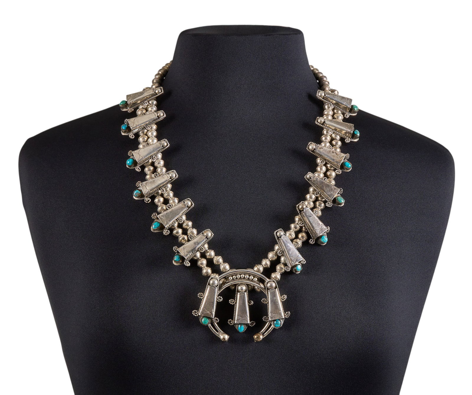 Sterling Silver & Turquoise Squash Blossom: Native American sterling silver squash blossom style necklace, set with turquoise cabochons in cradleboard motifs, with twisted wire details throughout, and hook and eye closure Length: 26 in. To